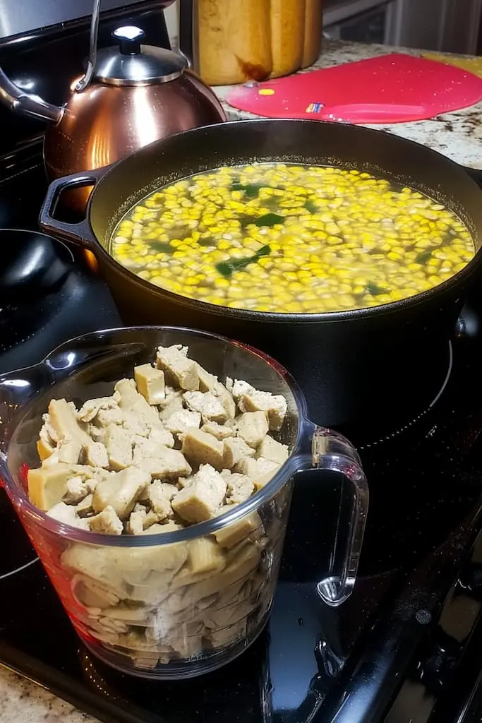 Cast iron skillet with simmering white beans and corn for vegetarian white chili, with cubed seitan in glass measuring cup ready to add