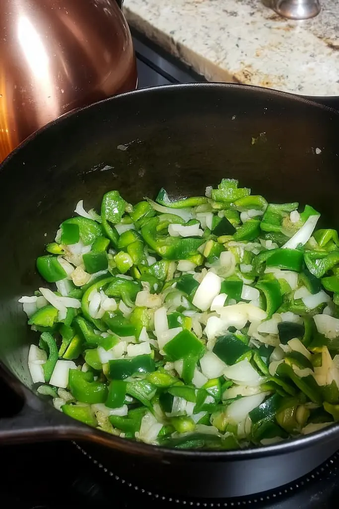 Chopped poblano peppers and diced onions sautéing in a black Dutch oven, the first step in making creamy vegetarian white chili.