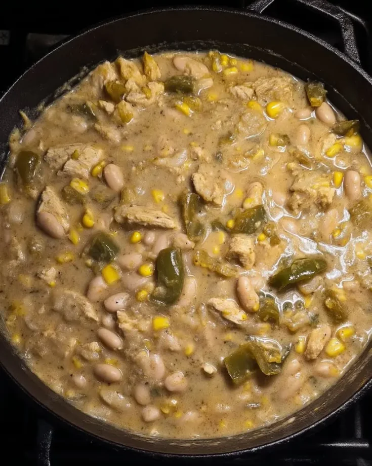 Creamy vegetarian white chili with white beans, corn, seitan, and green chilis simmering in a black cast iron pot