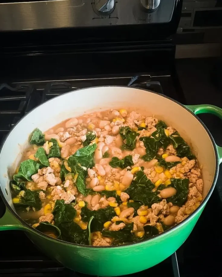 White bean chicken chili with Swiss chard and corn simmering in green Dutch oven on stovetop