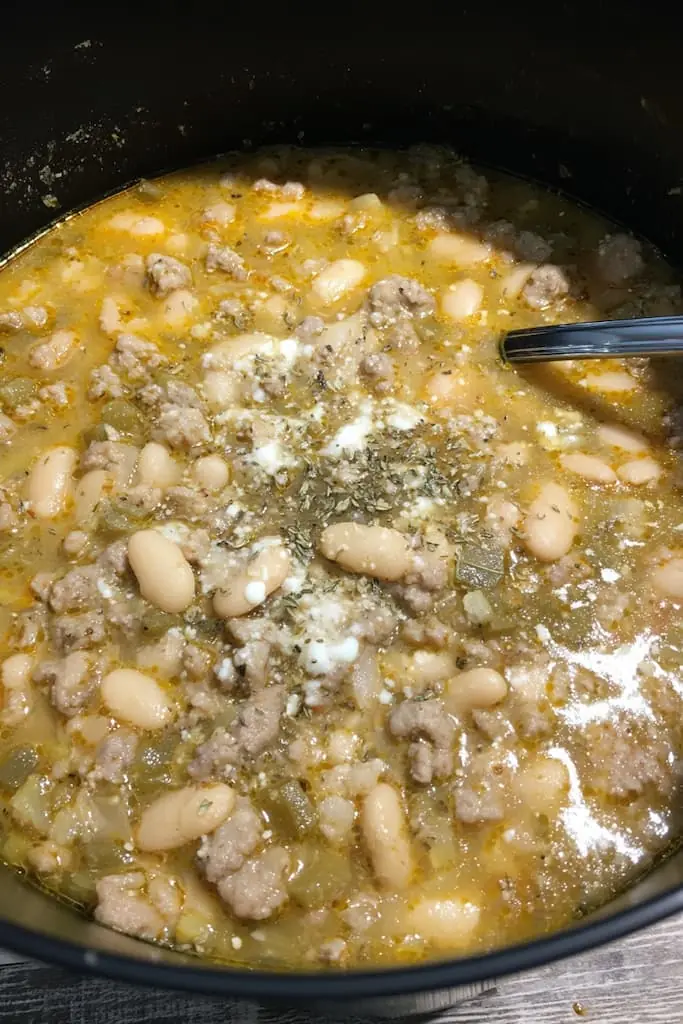 A pot of white chili with pork, white beans, green chiles, and melted cheese in a rich broth, served with a spoon.