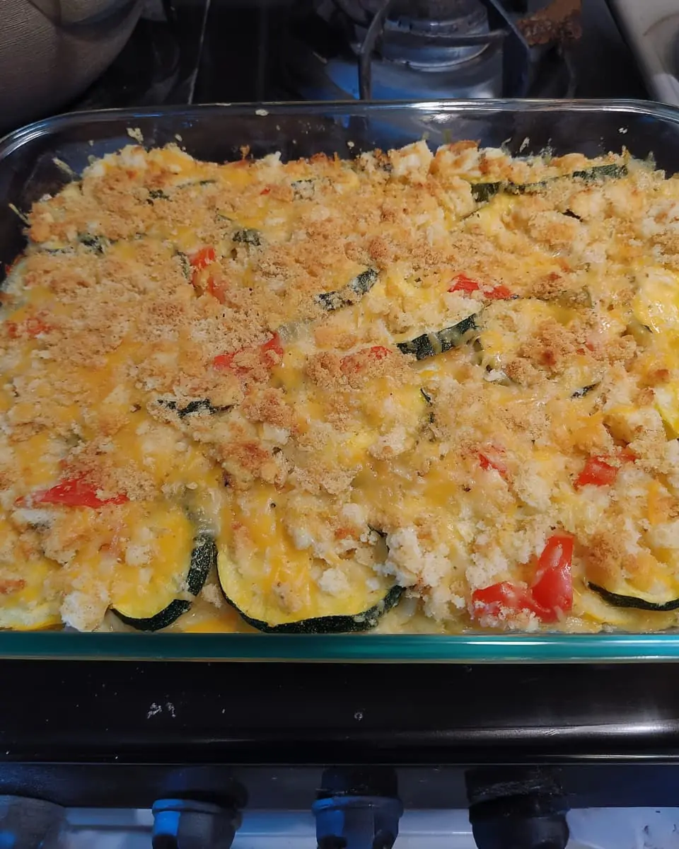 Baked zucchini and yellow squash casserole in a glass dish, topped with melted Cheddar and crisp buttery crumbs.
